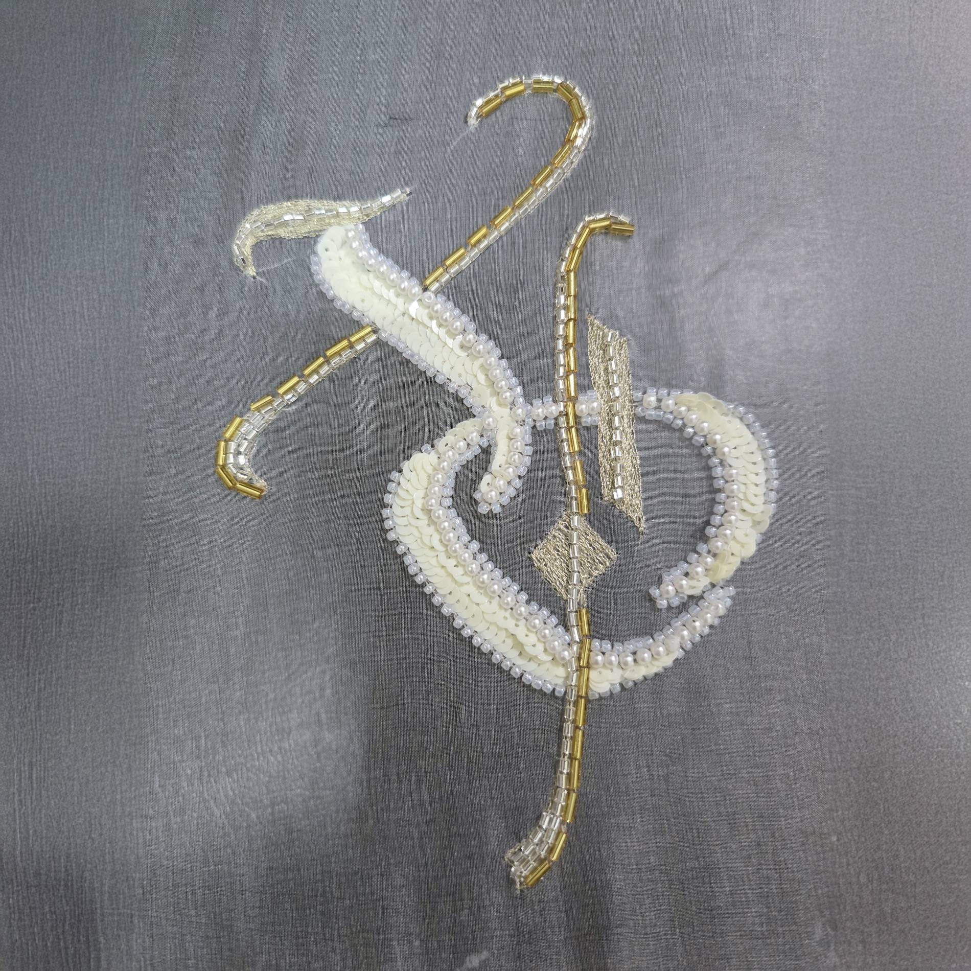Finished student work from a Lunéville embroidery course, featuring a stylised monogram embroidered with beads, sequins, and metallic thread on silk organza