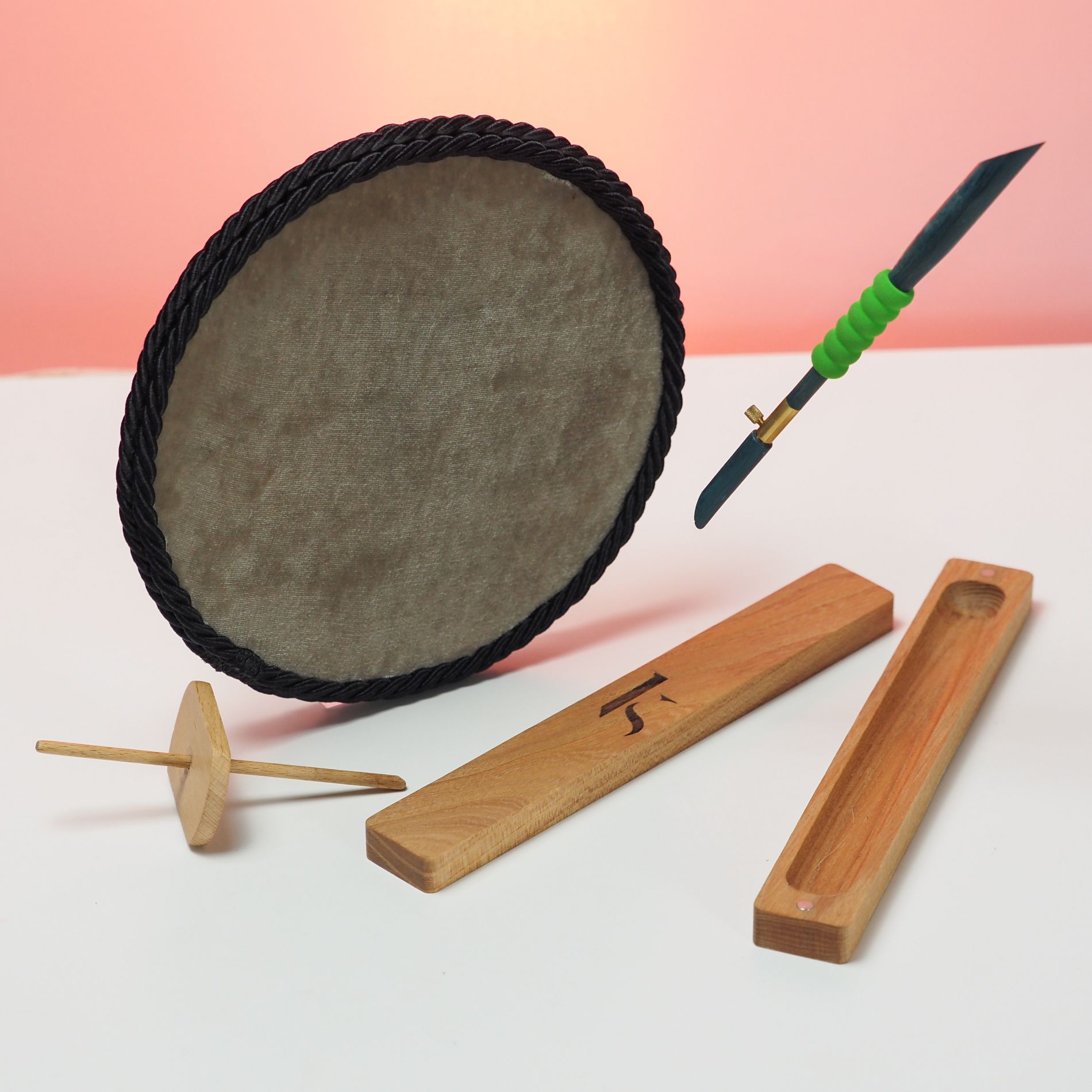 Round bead tray with cord edge, Luneville embroidery hook, and wooden tools displayed on a white surface with pink background.
