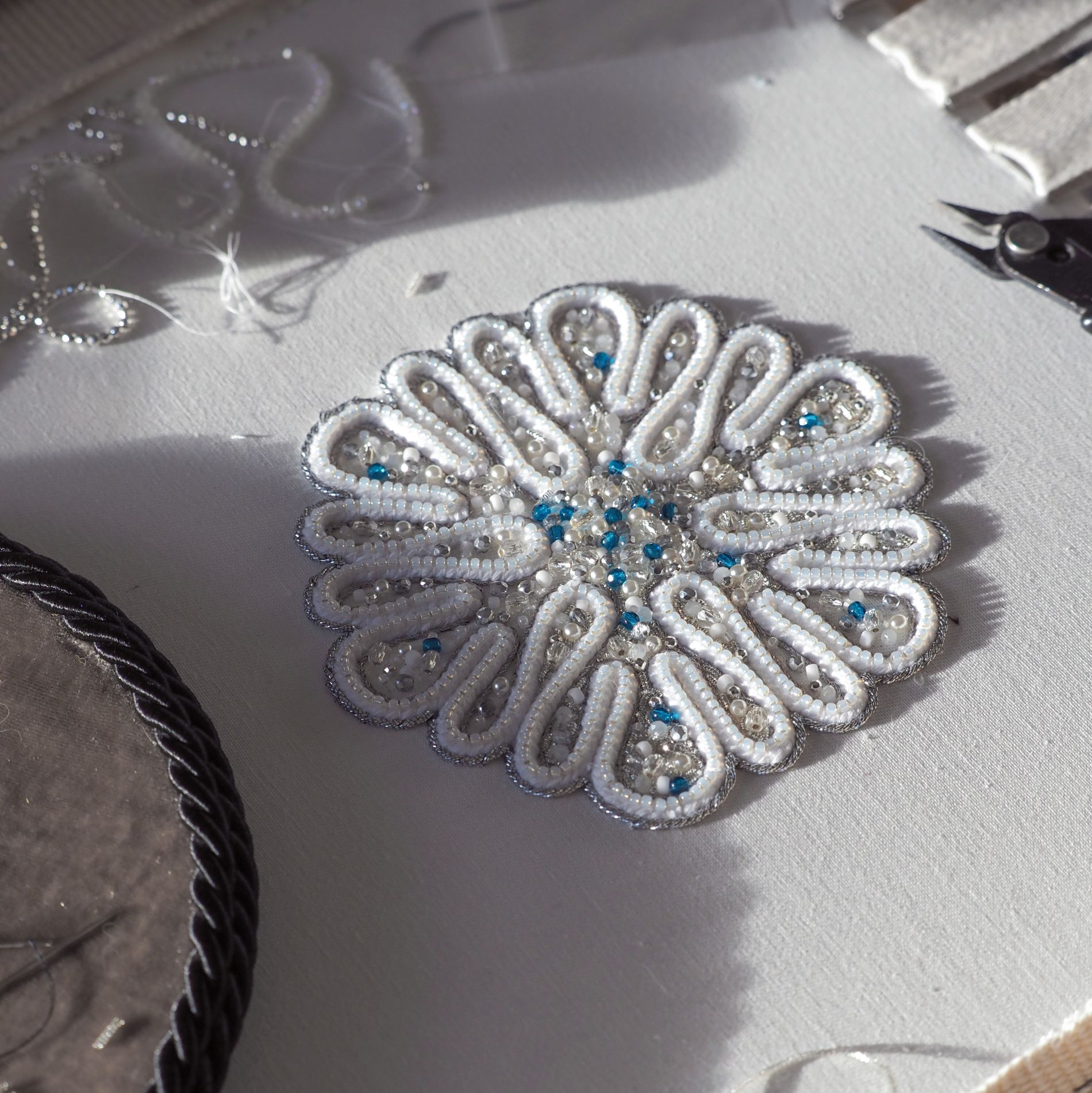 A behind-the-scenes view of the Jewels of Winter pearl embroidery project being completed on an embroidery frame. The photograph shows the handmade process, materials and detailed construction involved in creating the finished festive ornament.