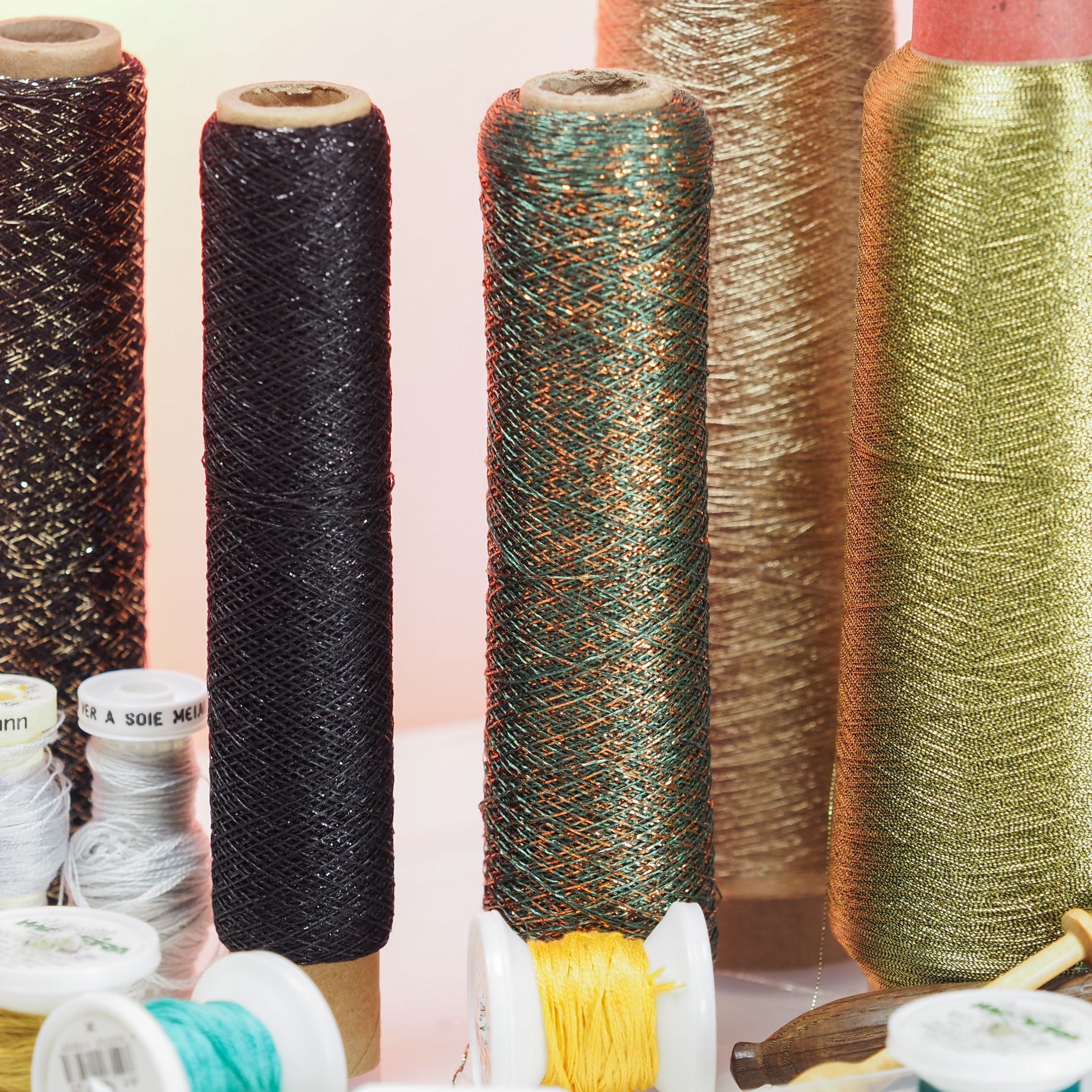 Close-up of metallic embroidery threads in black, green, gold, and copper tones with silk spools in bright and pastel colours