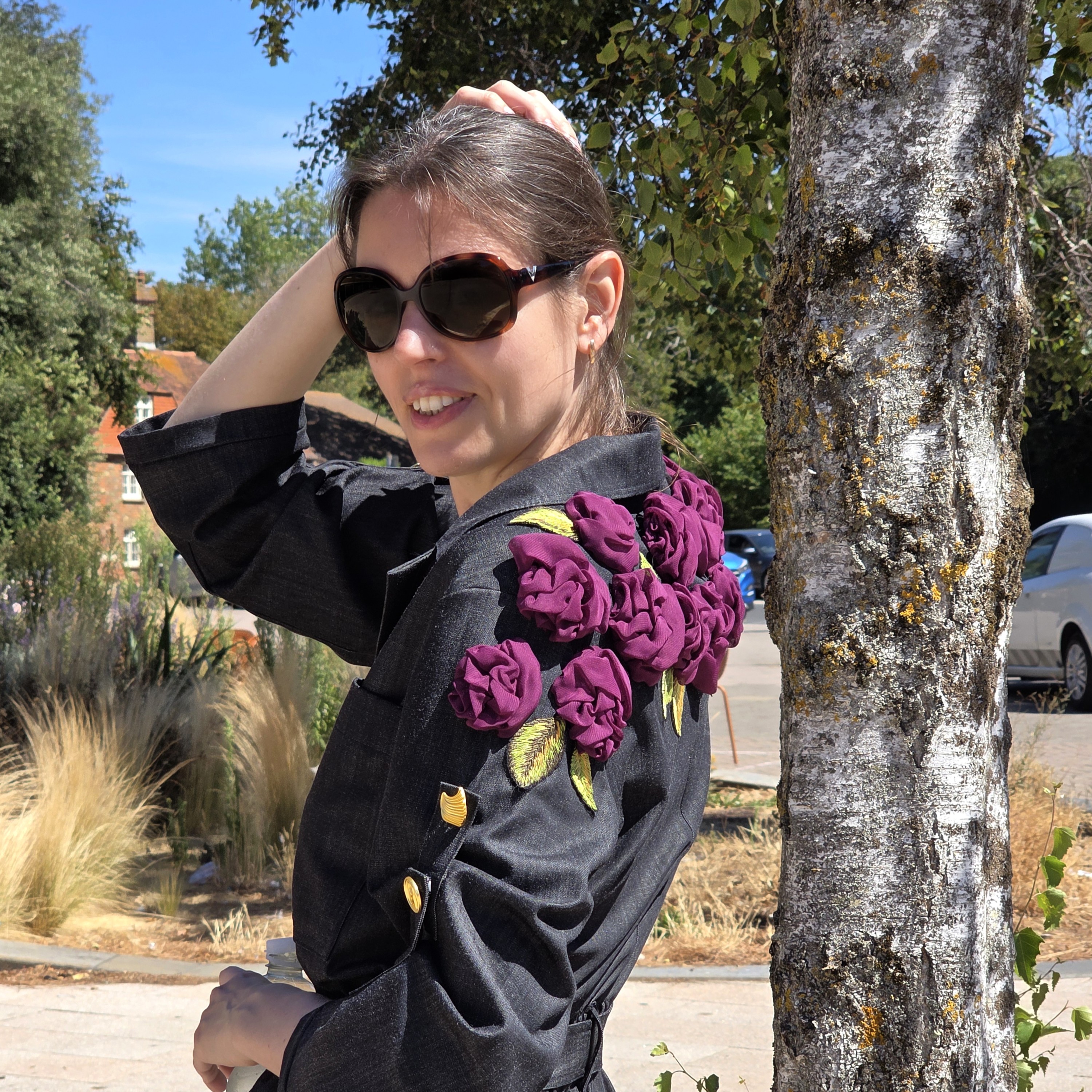 Side view of a black jumpsuit decorated over the shoulder with dimensional purple fabric roses and embroidered green leaves