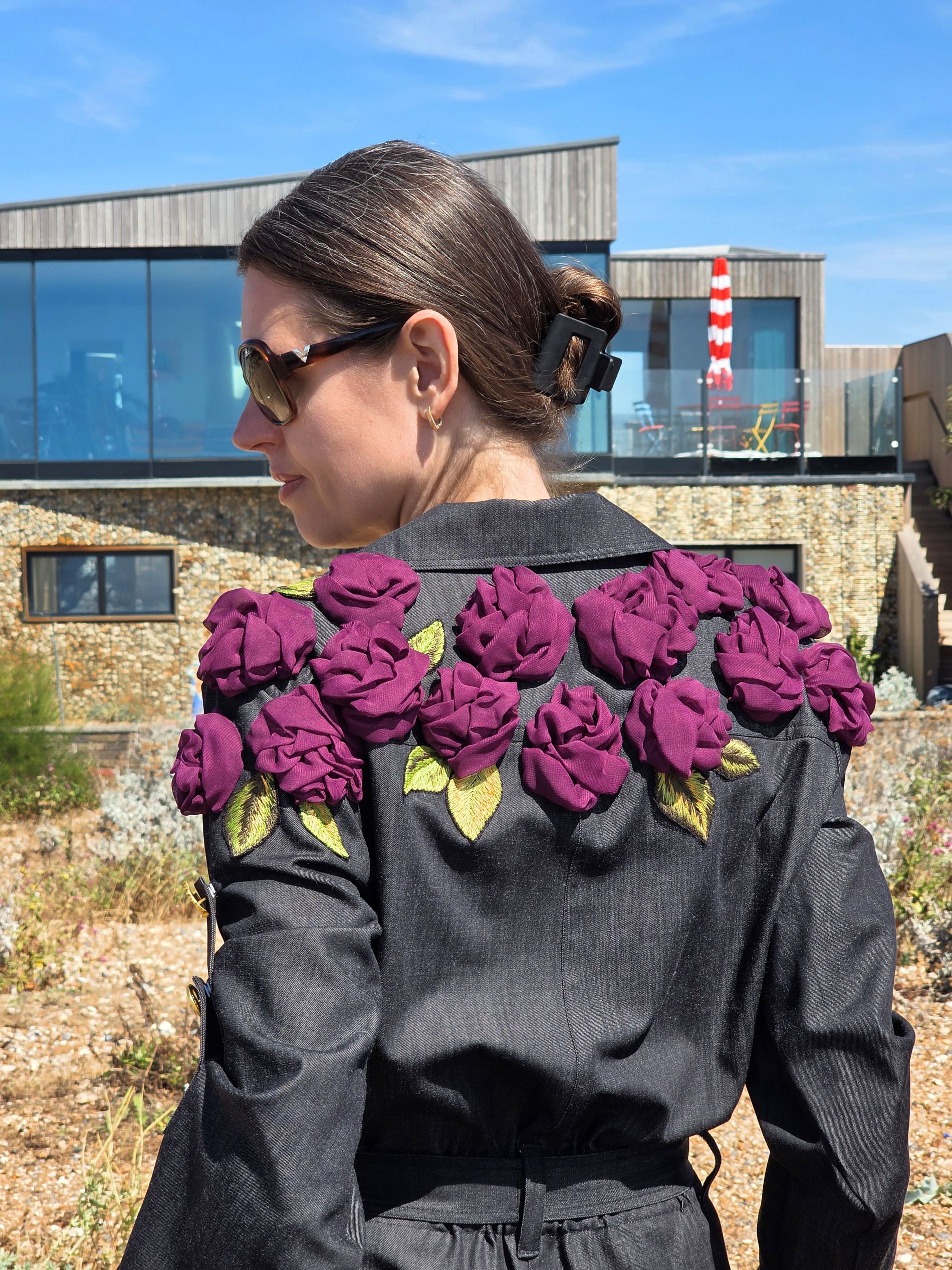 Back view of a black jumpsuit decorated across the shoulders with handmade purple fabric roses and embroidered leaves.