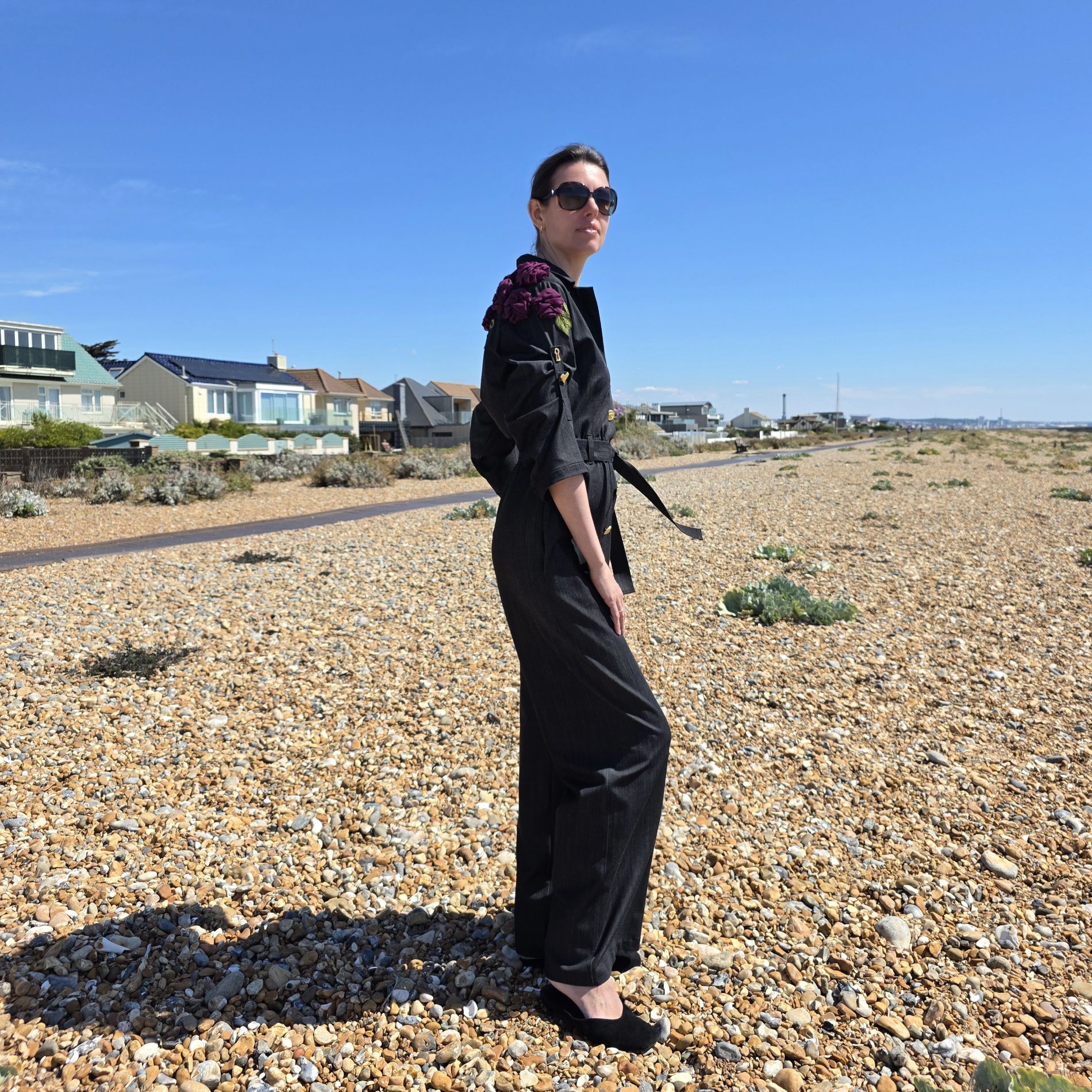 Full-length side view of a black belted jumpsuit with purple fabric roses decorating the shoulder and upper back.